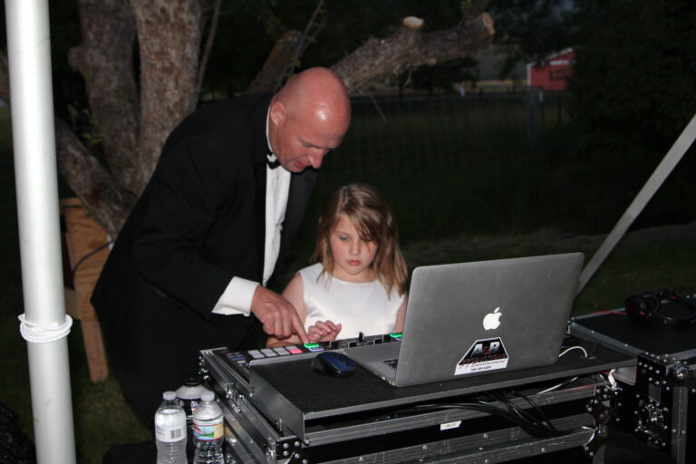 DJ and young girl at outdoor event with DJ equipment and laptop.