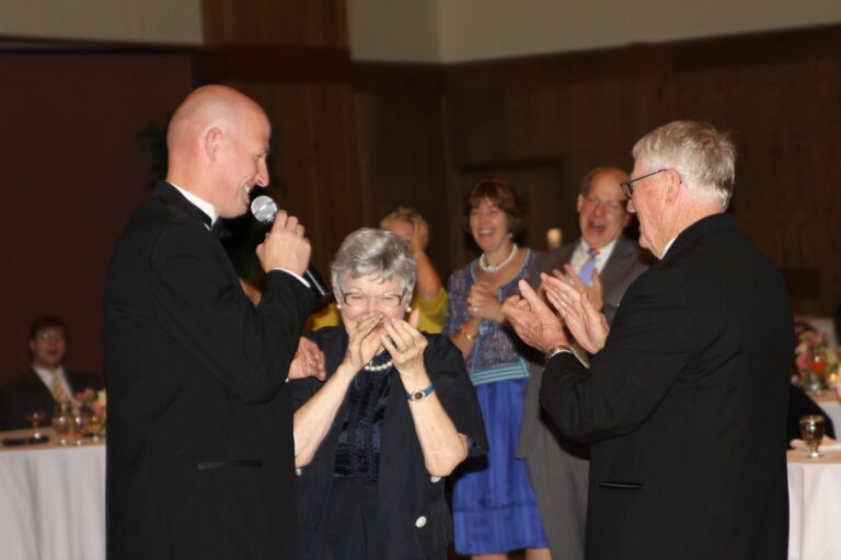Happy elderly woman receiving applause at A & B Productions celebration event.