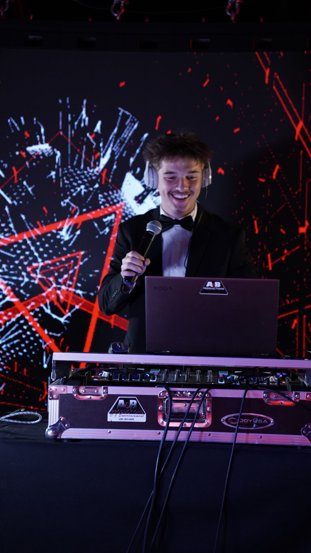 DJ performer at A & B Productions event with vibrant light display and DJ equipment.