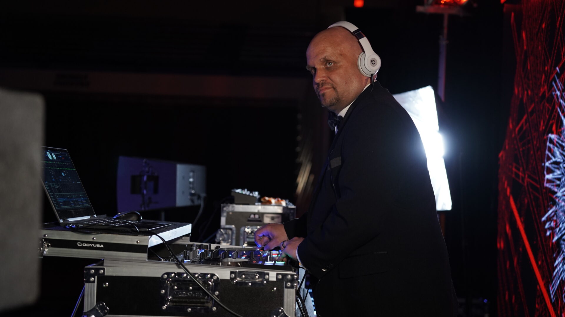DJ with headphones performing at a live event, showcasing professional sound equipment and lighting.