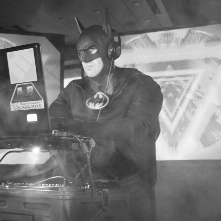 Batman dressed in costume, DJing at a live event with professional audio equipment.