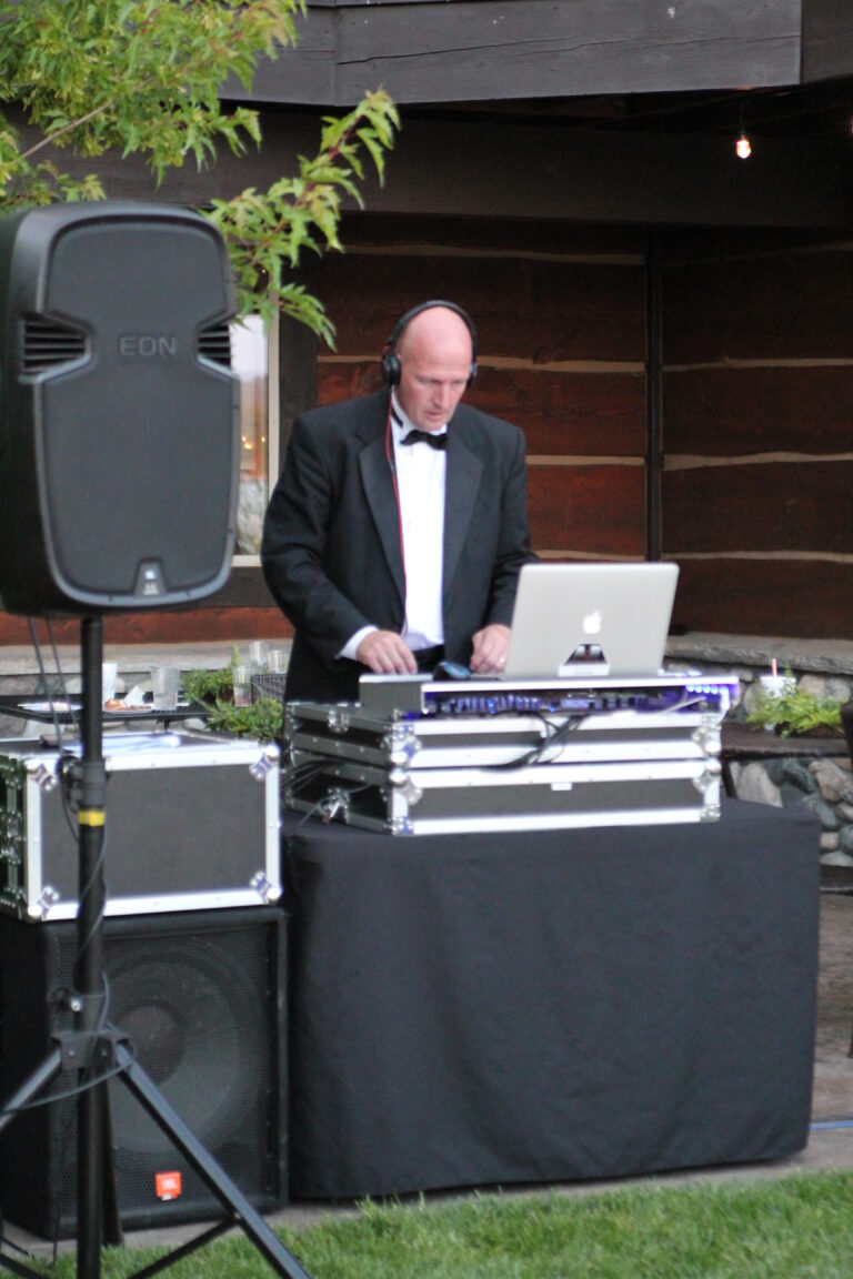 DJ in tuxedo with headphones working at outdoor event with sound system.