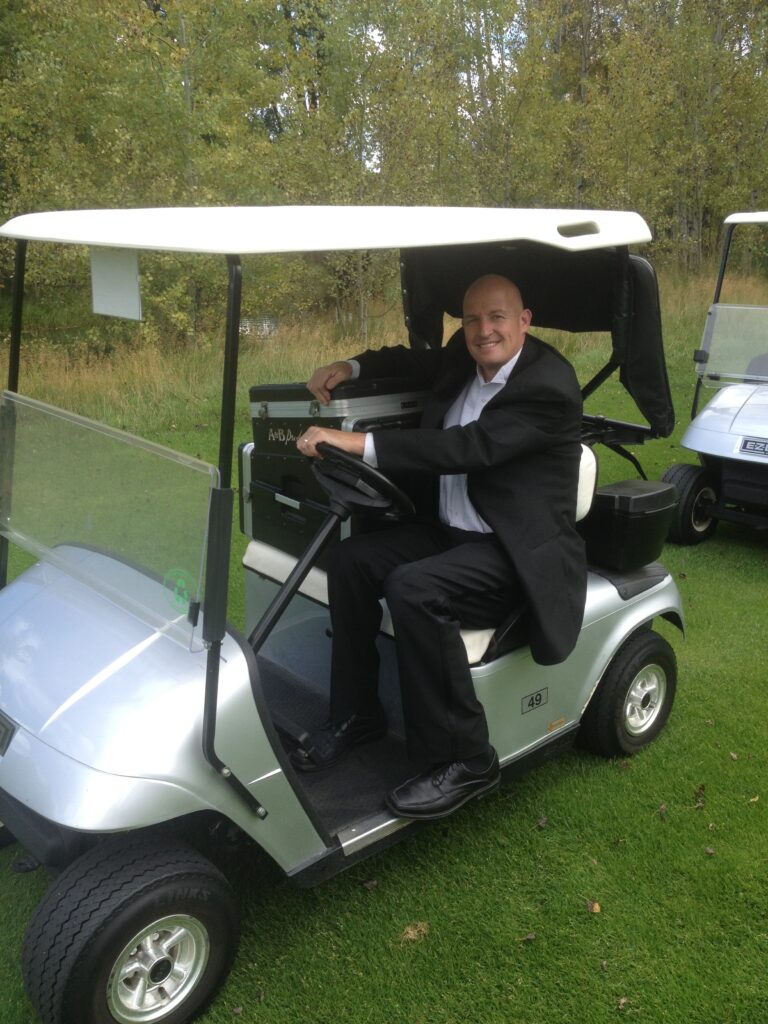 Man in suit riding a golf cart at A & B Productions event.