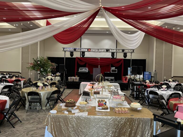 Elegant event setup with draped red and white fabric, stage, and decorated tables for a celebration.