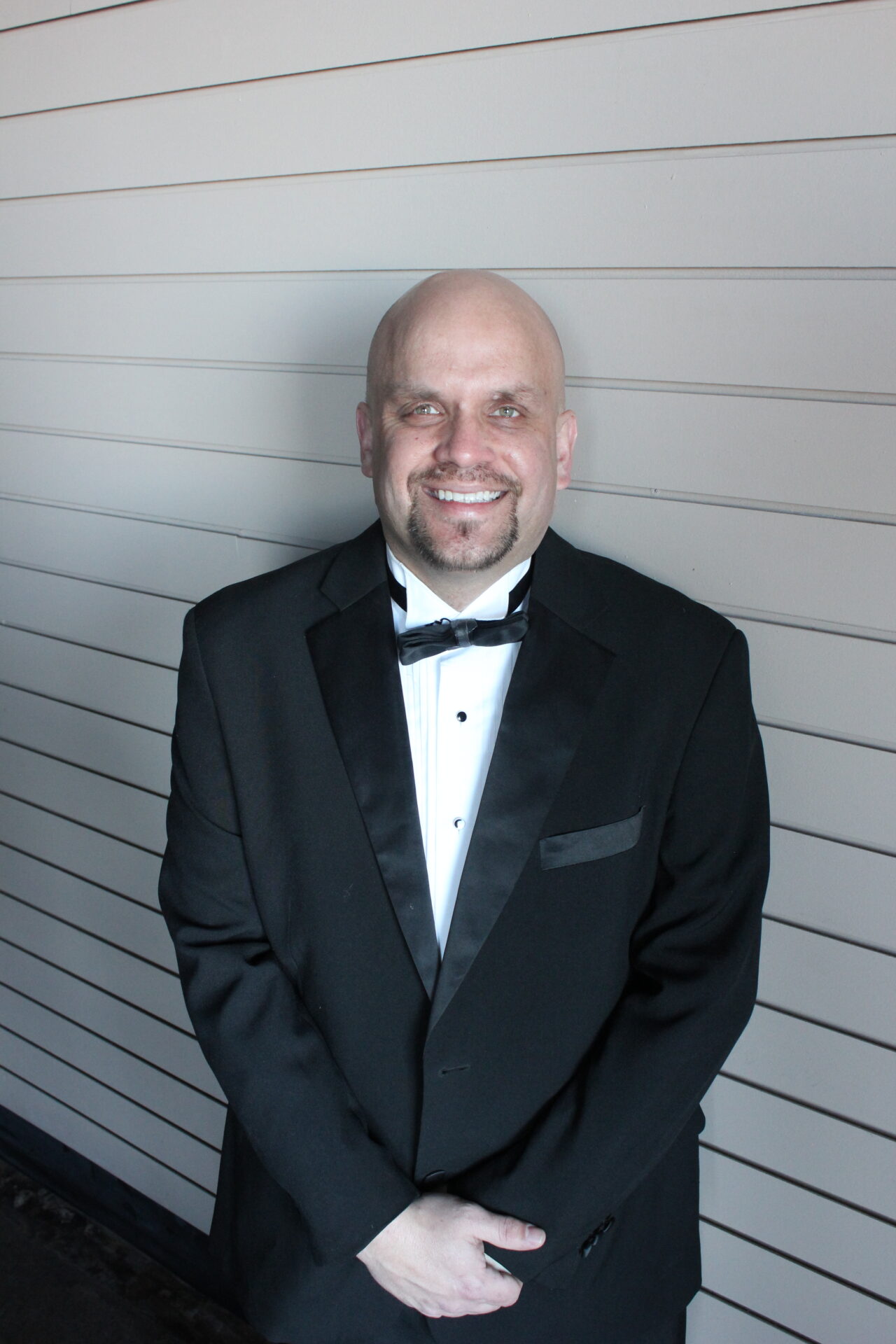 Professional male event host in tuxedo smiling at the camera.