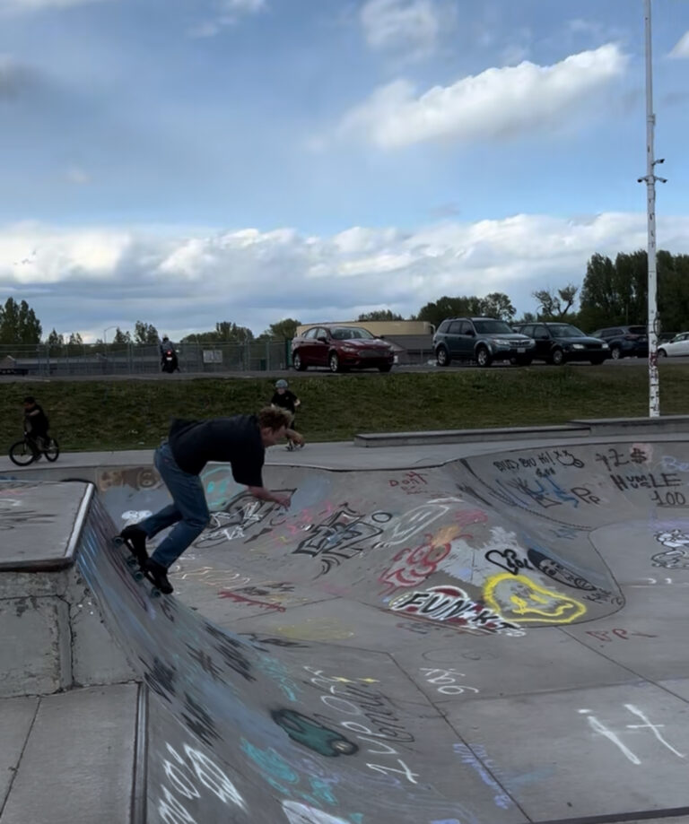 Skateboarder performing tricks at AbpDjs skatepark with graffiti-covered ramps.