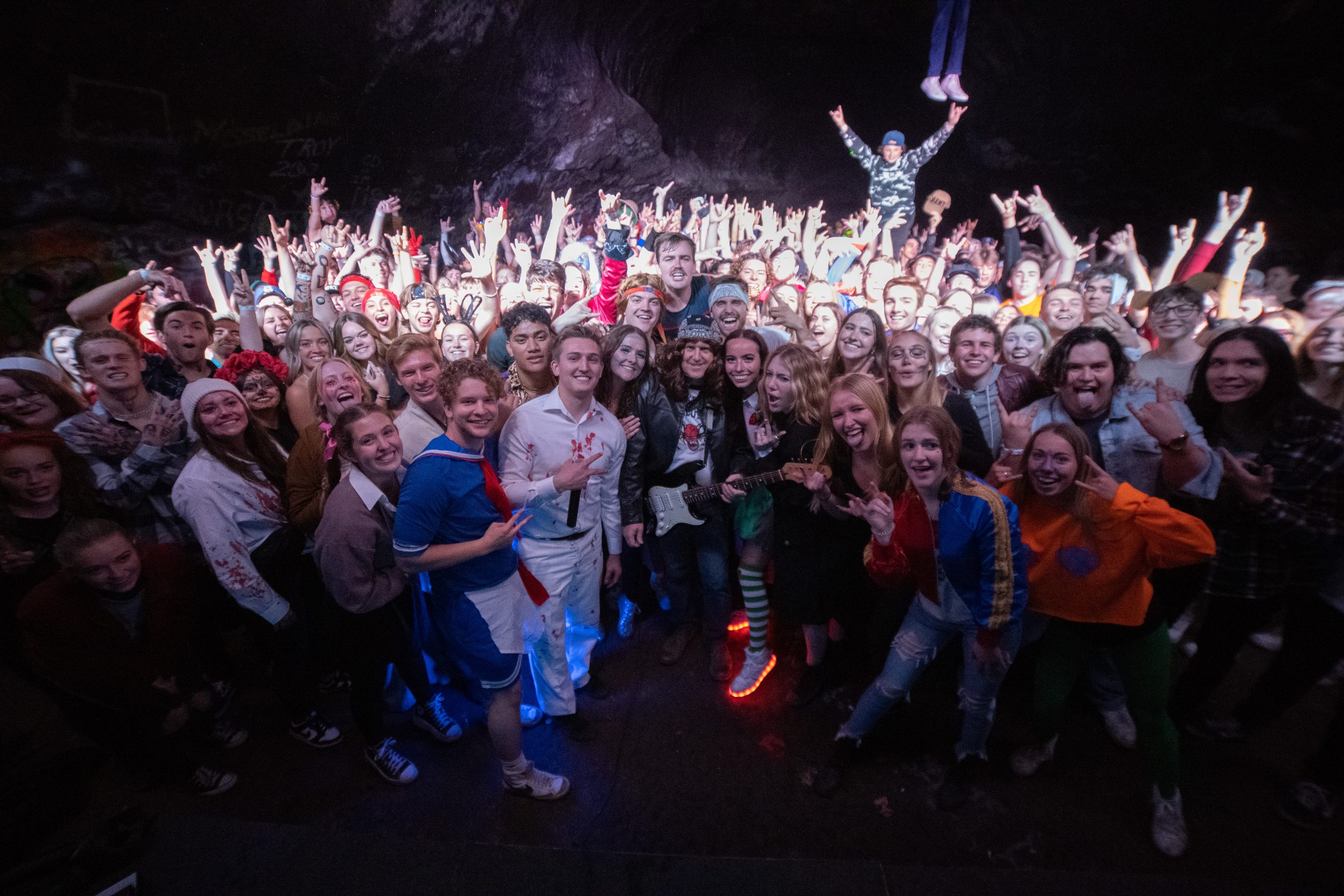 Big group photo of a party crowd cheering in a lit cave