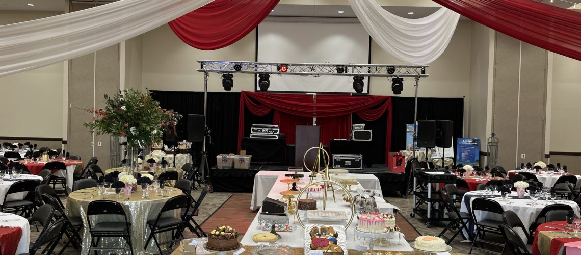 Elegant event setup with draped red and white fabric, stage, and decorated tables for a celebration.