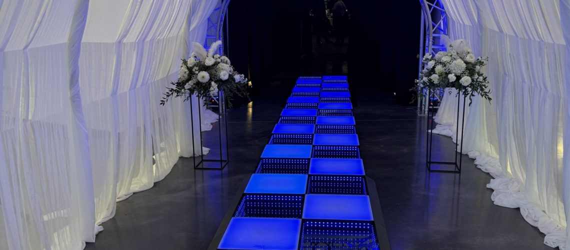 Modern event tunnel with illuminated blue walkway and floral decor by A & B Productions.
