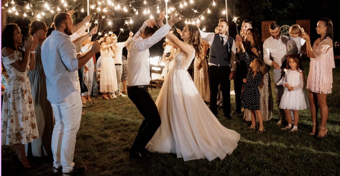 Couple dancing at wedding reception with guests and string lights.