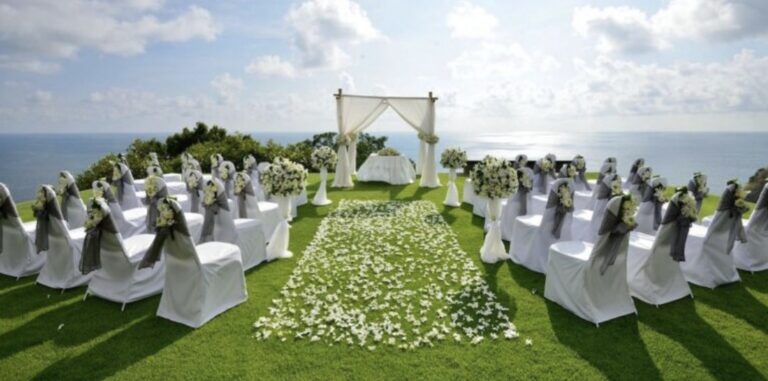 Elegant outdoor wedding setup on a grassy area by the sea with floral decorations.