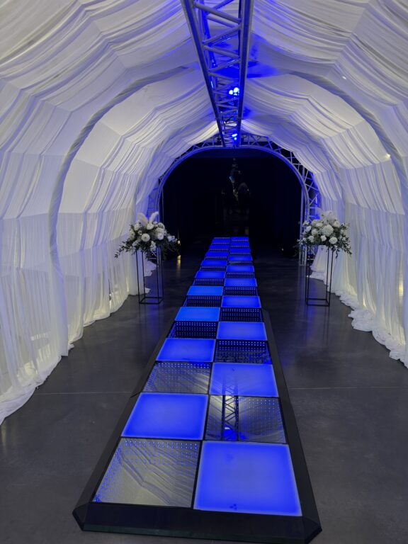 Modern event tunnel with illuminated blue walkway and floral decor by A & B Productions.